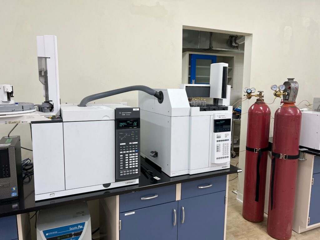 Testing lab environment featuring Agilent gas chromatography systems on a benchtop with connected gas cylinders.